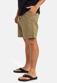 Shorts khaki en tissu léger, dotés de poches latérales et d'une coupe droite, associés à des tongs noires.