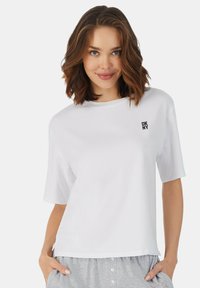 Witte korte mouw t-shirt met een ronde halslijn en klein zwart DKNY-logo op de linkerbovenborst, gemaakt van een zachte, lichte stof.
