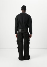Zwart langemouwen shirt gecombineerd met donkere cargo pants met meerdere zakken, een losse pasvorm en een gestructureerde tailleband met logo detail.