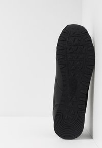 Fekete sneaker, textúrált gumitalppal, háromszögletű mintával, sima felső része van. Minimalista dizájn.