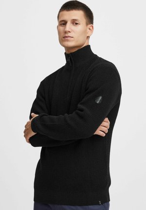 Schwarzer Zip-Pullover aus strukturiertem Strickstoff, mit gerippten Bündchen und Saum, sowie einem Logo-Akzent am linken Ärmel.