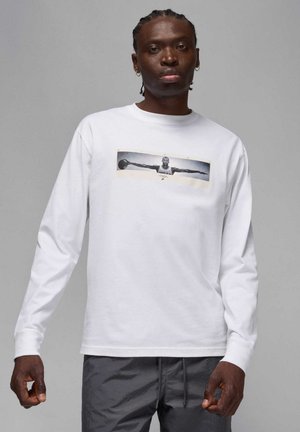 Camiseta blanca de manga larga con un estampado gráfico en el centro que muestra a un jugador de baloncesto. Tejido de algodón suave, ajuste holgado, cuello redondo.