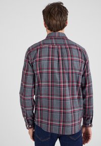 Grijze geruite blouse met rode en zwarte accenten, lange mouwen, knopen bij de manchetten en een afgeronde zoom. Gemaakt van een zachte, gestructureerde stof.