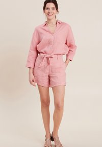 Completo in lino rosa composto da una camicia con bottoni e pantaloni shorts con cintura. I dettagli notevoli includono una tasca sul petto e orli dei pantaloni shorts arrotolati.