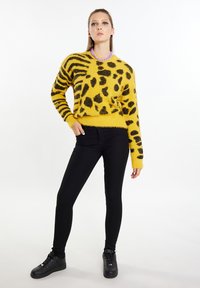 Pulover galben pufoș cu imprimeu leopard negru; mâneci lungi și un tiv ajustat. Purtați cu blugi skinny negri și adidași negri.