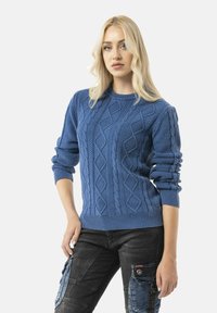 Pull en tricot bleu avec un motif en câble texturé, des poignets et un ourlet côtelés, présentant un col rond et des manches légèrement retroussées.