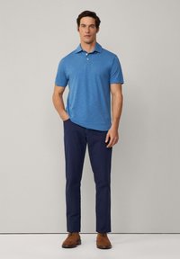 Modrá polo tričko s krátkým rukávem vyrobené z texturované látky, spárované s tmavě modrými kalhotami a hnědými botami. Tričko má klasický límeček a knoflíky.