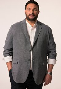 Szary, strukturalny żakiet z klapami, dwoma czarnymi guzikami, kieszenią na piersi i podwiniętymi rękawami na białej koszuli; widoczne ciemne spodnie i zegarek.