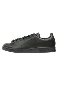Sorte lædersneakers med en glat tekstur, rund tå, flad gummisål, syv snørrehuller og sidelufthuller til ventilation.