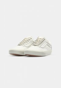 White canvas sneakers with a low profile, round toe, textured sole, and contrasting side stripe; laced with six eyelets and padded collar.