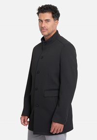 Abrigo negro ajustado hecho de tela texturizada; cuenta con un cuello alto, botones frontales y bolsillos laterales.