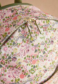 Rucksack mit Reißverschluss, der ein florales und geometrisches Muster in Pink, Grün und Creme zeigt. Goldene Reißverschlussbeschläge ergänzen das Design.