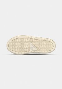 Rubber sneaker sole with a textured, triangular grip pattern. Cream-colored with a logo detail near the heel and a reinforced toe section.