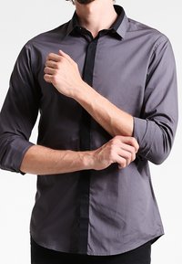 Grijze langemouwen shirt met een zwarte knoopsluiting, gestructureerde kraag en knoopmanchetten. Gladde stof met een subtiele glans en op maat gemaakte pasvorm.