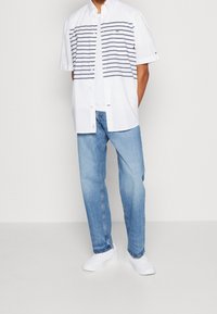 Vit t-shirt med kort ärm och horisontella blå ränder, kombinerad med ljusblå denimjeans och vita sneakers. Avslappnad passform och klassisk design.