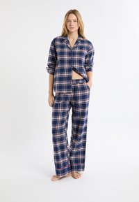 Granatowy zestaw piżam w kratę wykonany z miękkiego materiału; zawiera koszulę na guziki z podwiniętymi rękawami oraz luźne spodnie z czerwonym akcentem na obszyciu.