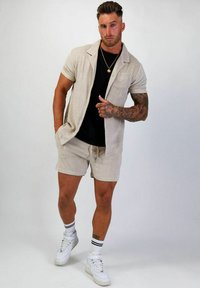 Beige linne skjorta med kort ärm i kombination med matchande shorts. Svart T-shirt under. Vita högskor med svarta randiga strumpor.