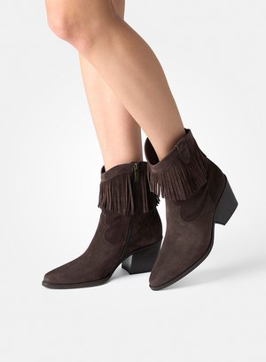 Jambes portant des bottines en daim marron foncé avec bordure à franges, fermeture éclair latérale et talons moyens épais sur fond blanc.