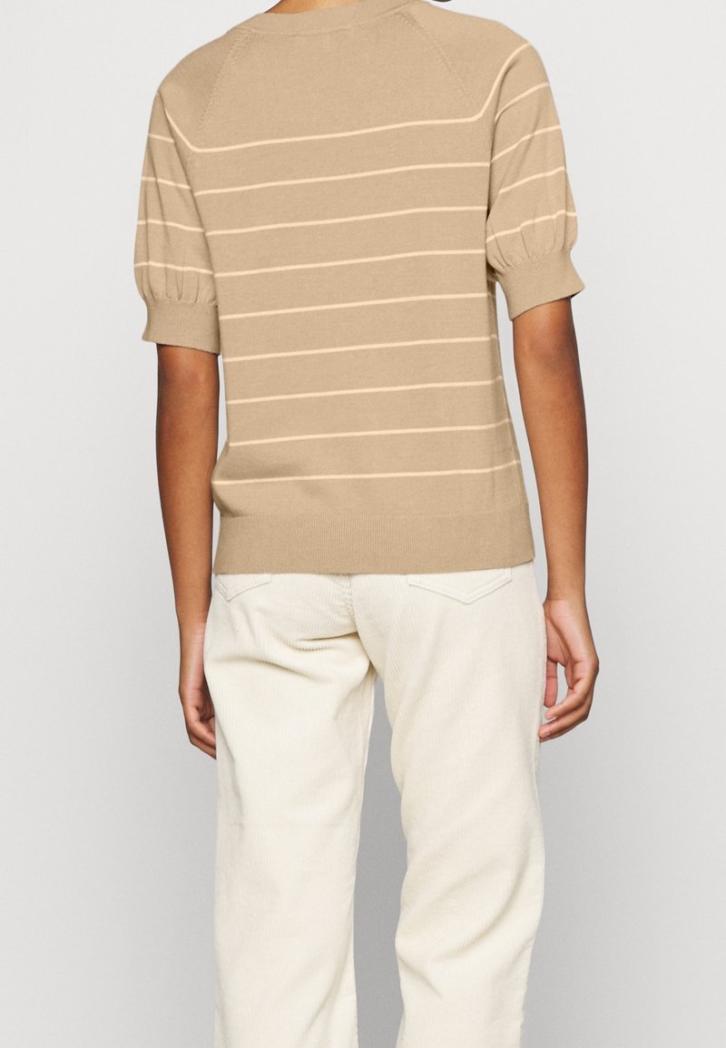 Beige striktrøje med horisontale cremefarvede striber, korte puffærmer og ribbet kant, parret med off-white fløjl bukser.