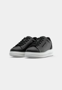 Sneakers negri din piele cu talpă din cauciuc alb. Caracteristici includ închidere cu șireturi, vârf rotunjit și logo aproape de toc. Design simplu, modern.