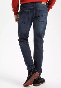 Granatowe dżinsy o slim fit, z tylnymi kieszeniami i skórzaną łatą na pasku. W zestawie z czarnymi butami.