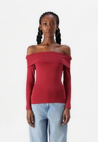 Raudonas ilgomis rankovėmis of off-the-shoulder topas, prigludęs dizainas, medvilnės medžiaga, lygus paviršius, plati iškirptė ir pritaikytos rankovės, dėvimas su džinsais.