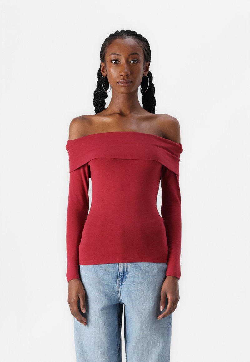 Raudonas ilgomis rankovėmis of off-the-shoulder topas, prigludęs dizainas, medvilnės medžiaga, lygus paviršius, plati iškirptė ir pritaikytos rankovės, dėvimas su džinsais.