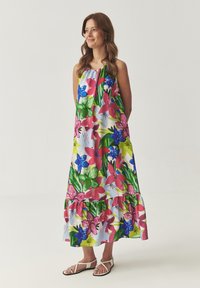 Robe maxi florale dans des teintes vives de rose, bleu et vert, avec un ourlet en étages et une coupe décontractée, fabriquée en tissu léger. Des sandales complètent le look.