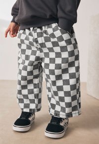 Črno-bele kariraste hlače z ohlapnim krojem, narejene iz mehke tkanine, kombinirane s črnimi in belimi vzorčastimi supergami.