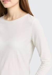 Lange mouwen, crème kleurige top van een gladde, rekbare stof. Voorzien van een ronde halslijn en een aangesloten silhouet, ideaal om in laagjes te dragen.