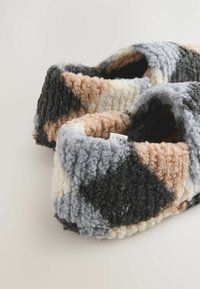 Teksturowane kapcie z wzorem patchworkowym w pastelowych odcieniach brzoskwini, szarości i czerni, wykonane z miękkiego, puszystego materiału dla wygody.