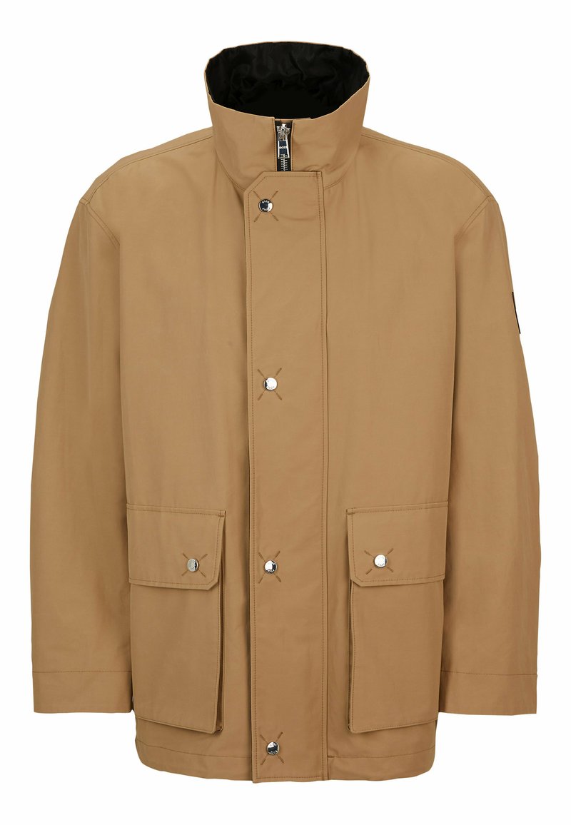 Tan wasserfeste Jacke mit hohem Kragen, silbernen Druckknöpfen, zwei Fronttaschen und einer glatten, matten Oberfläche. Innenfutter ist schwarz.