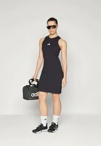 Pieguloša melna sporta kleita ar augstu kakla izgriezumu; rotāta ar mazu baltu Adidas logotipu. Aksesuāri ietver melnus saulesbrilles un melnu sporta somu.