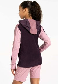 Fleece-Hoodie in Dunkelpurpur mit pinken Ärmeln und Kapuze. Verfügt über einen Reißverschluss und ein strukturiertes Material. Kombiniert mit pinken Shorts.