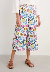 Floral-patterned, wide-leg culottes in white, featuring pink, yellow, and blue flowers with green leaves; paired with brown strappy sandals.