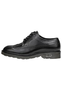 Scarpa brogue nera in pelle con perforazioni decorative, punta rotonda e suola in gomma grigia. Presenta sei occhielli e un accento con marchio sul lato.