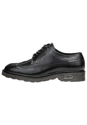 Scarpa brogue nera in pelle con perforazioni decorative, punta rotonda e suola in gomma grigia. Presenta sei occhielli e un accento con marchio sul lato.