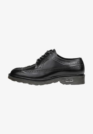 Scarpa brogue nera in pelle con perforazioni decorative, punta rotonda e suola in gomma grigia. Presenta sei occhielli e un accento con marchio sul lato.