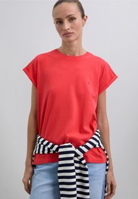 Red cotton t-shirt with rolled sleeves, paired with a striped navy and white cotton tie around the waist. Simple, casual design.