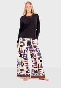 Black long-sleeve V-neck top with a layered neckline. Wide-leg pants feature a colorful geometric pattern in red, blue, and black on a cream background.