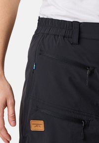 Zwarte cargoshorts met een elastische tailleband, ritszakken en een tan leren merkembleem. Voorzien van een kleine blauwe en gele accent.
