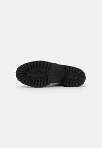Semelle de botte en caoutchouc noir avec des rainures profondes pour la traction. Logo notable embossé sur la semelle intermédiaire, forme arrondie de la pointe, surface texturée.