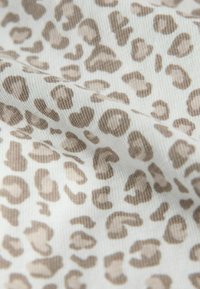 Tkanina w wzór panterki z plamami w różnych odcieniach brązu na białym tle, o teksturowanej, prążkowanej powierzchni.