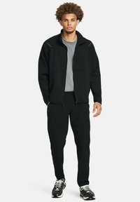 Černá zipová bunda s šedým tričkem, odpovídajícími černými kalhotami a černými teniskami. Obsahuje kapsy a má uvolněný střih.