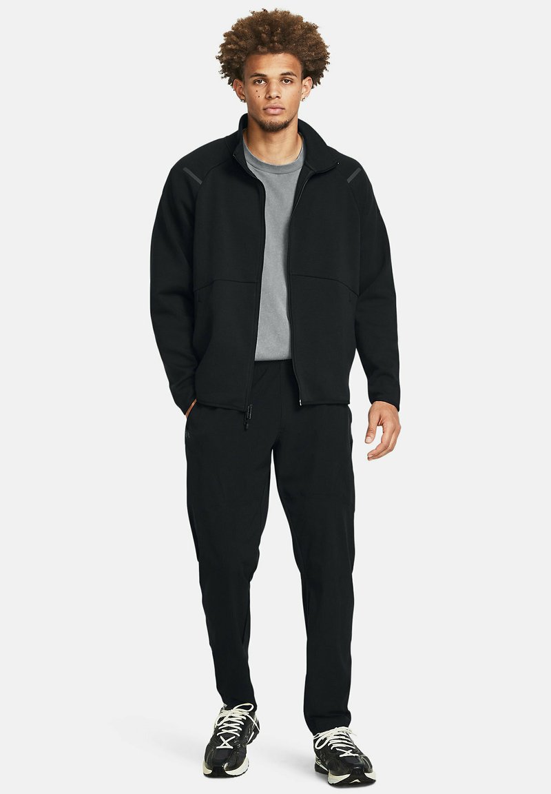 Czarna kurtka z zamkiem błyskawicznym, szary T-shirt, pasujące czarne spodnie i czarne trampki. Posiada kieszenie i luźny krój.