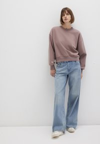 Oversized mauve sweatshirt with a wide crew neckline and ribbed hem, paired with light blue flared jeans featuring a classic five-pocket design.
