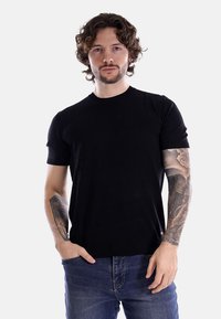 T-shirt nera a maniche corte in maglia con scollatura rotonda, design aderente e texture liscia, abbinata a jeans blu.