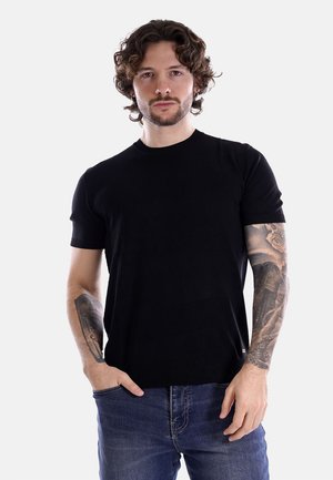 T-shirt nera a maniche corte in maglia con scollatura rotonda, design aderente e texture liscia, abbinata a jeans blu.