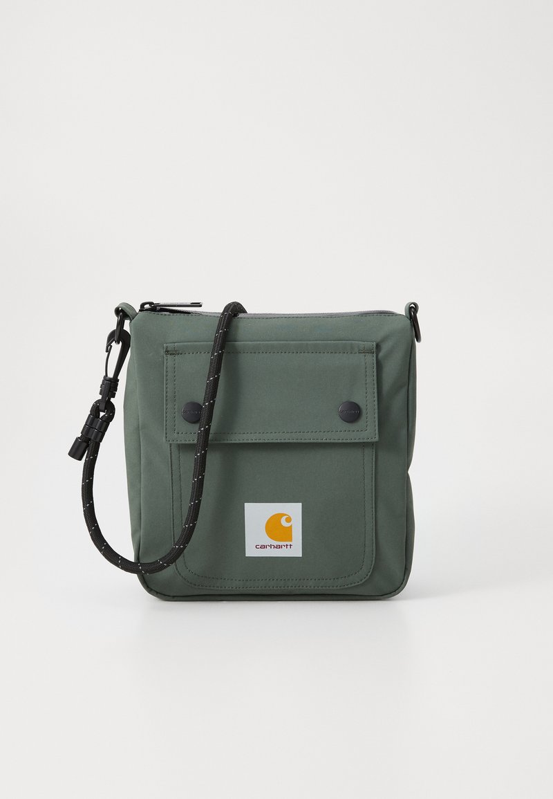 Borsa a tracolla verde in tessuto con chiusura a zip, tasca frontale con patta, tracolla nera regolabile e una patch con logo sulla parte frontale.