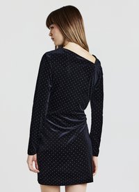 Schwarzes Samtkleid mit langen Ärmeln, weiße Polka-Dots, Ausschnitt am Rücken und gerafftes Design in der Taille. Glatte Textur.